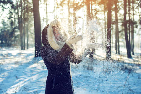 attractive woman in winter on a walk in the woods smiling throws up snow into the air at sunset, the concept of a cozy winter vacationの写真素材