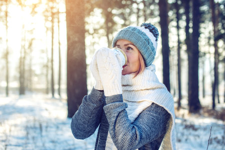 attractive woman in winter, a knitted sweater, mittens and scarf, walking through the Park among the...