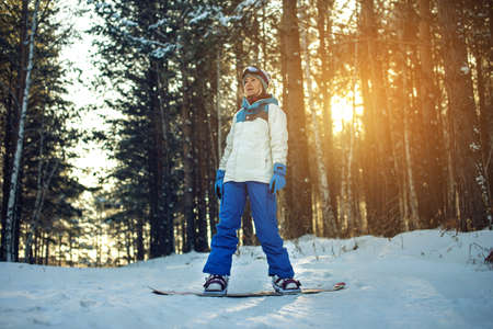 female snowboarder snowboarding down the mountain among the trees at sunset, concept of sport and active lifestyleの写真素材