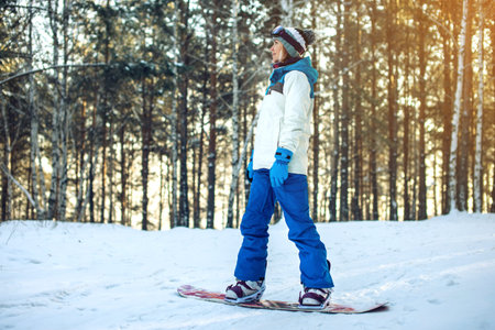 female snowboarder snowboarding down the mountain among the trees at sunset, concept of sport and...