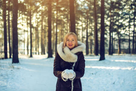 attractive woman in winter on a walk in the woods smiling throws up snow into the air at sunset, the concept of a cozy winter vacationの写真素材