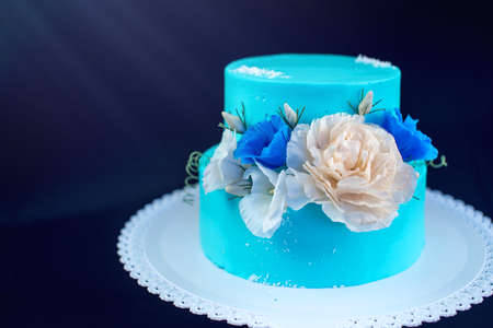 Beautiful blue like ice a wedding cake decorated with large roses on a dark background, concept wedding dessertsの写真素材