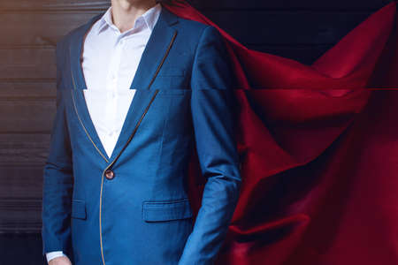 Superman. businessman standing in a suit and red cloak like a superhero on a dark background. the concept of progress in your careerの写真素材