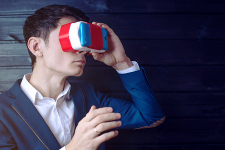 Attractive Young businessman in suit uses a colorful virtual reality glasses on a dark wooden...