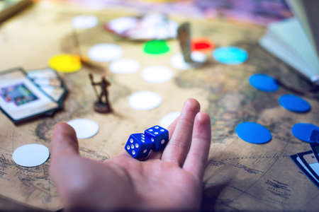 hand throws the dice on the background blurred colorful fantasy world map Board games, gaming moments in dynamics