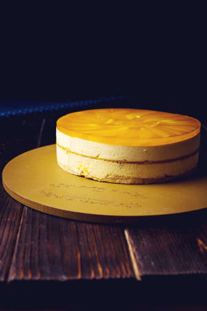 delicious multi-layered fruit mango cake stands on a circular base on a wooden table and dark background. food design. place for textの写真素材