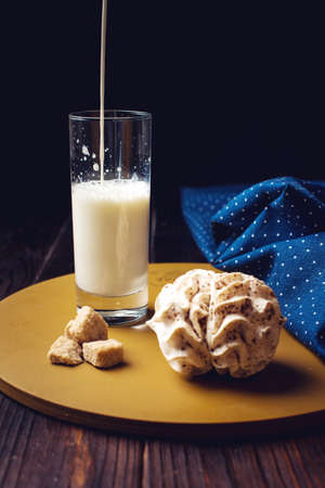 milk pouring into a glass on a wooden table next to the marshmallow and sugar cube on a dark backgroundの写真素材