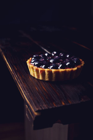 On mini Berry tart with blueberries on a wooden table over dark backgroundの写真素材