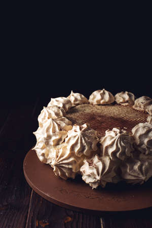 Beautiful white Meringue cake, sprinkled with cocoa stands on a wooden table over dark backgroundの写真素材