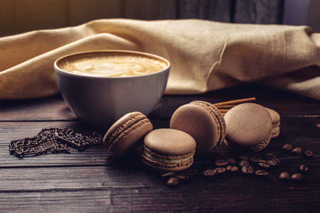 Flavored coffee cappuccino with beautiful foam is on the dark wooden table with macarons and chocolate in the shape of a heart. The perfect Breakfast for Valentine's dayの写真素材