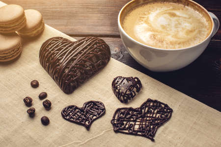 Flavored coffee cappuccino with beautiful foam with macarons and chocolate in the shape of a heart. The perfect Breakfast for Valentine's dayの写真素材