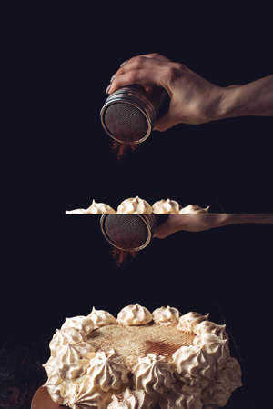 Hand sprinkle cocoa on the Beautiful white cake, a wooden table over dark backgroundの写真素材