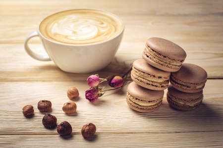 Flavored coffee cappuccino with beautiful foam is on the light wooden table with macarons and nuts. The perfect morning Breakfast for Valentine's dayの写真素材