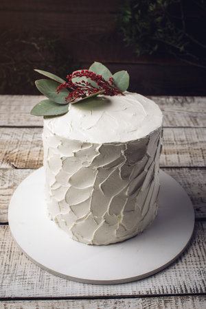 white cream cake decorated with green leaves of the eucalyptus tree on a wooden stand in a rustic style. trends for wedding desserts, foot designの写真素材