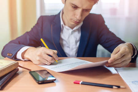 Man businessman signs documents with a pen making the signature sitting at the desk in the light. With retro effect.の写真素材