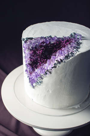 Artwork. Wedding cake decorated with white cream and purple stones like amethyst in a cut on a background of wavy fabric. food design. trendsの写真素材