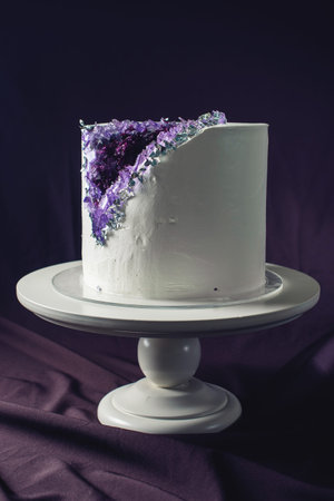 Artwork. Wedding cake decorated with white cream and purple stones like amethyst in a cut on a background of wavy fabric. food design. trendsの写真素材