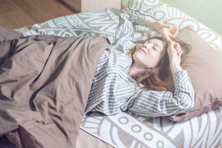 Attractive girl waking up early in the morning, lying sleepy in bed and nice with a smile stretching