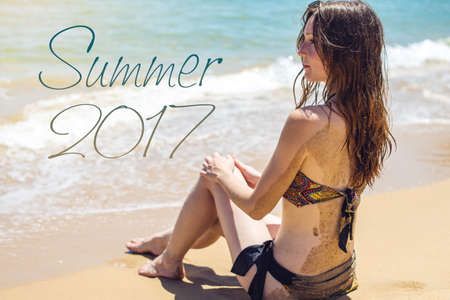 Woman in swimsuit sitting on the sandy beach and looks out to sea. The summer of 2017. The concept of Paradiseの写真素材