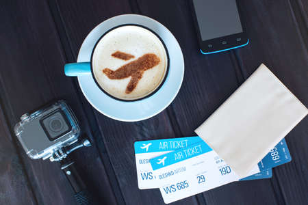 Cup of coffee with the airplane of cinnamon on foam next to tickets, passport, phone and a gopro camera on the background map of the world. Traveling conceptの写真素材