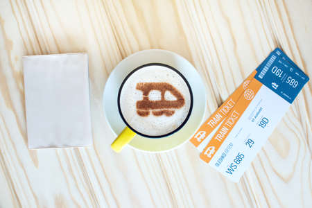 Cup of coffee with the train of cinnamon on foam next to tickets, passport on the background map of the world. Traveling conceptの写真素材
