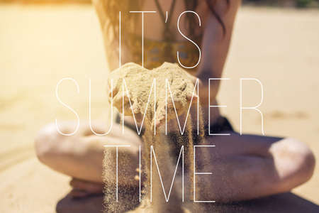 Woman sitting on beach by the sea and holds the sand that pours beautifullyの写真素材