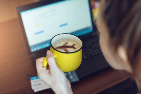 Woman holds in her hands a Cup of coffee with the plane of the cinnamon working at a laptop and to...