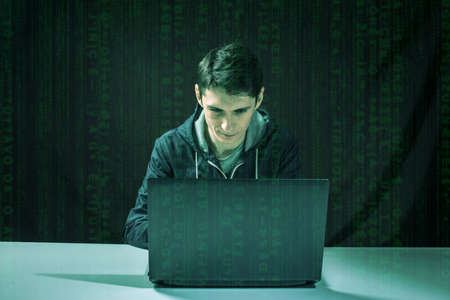 young hacker in the dark breaks the access to steal information and infect computers and systems. concept of hacking and cyber terrorismの写真素材