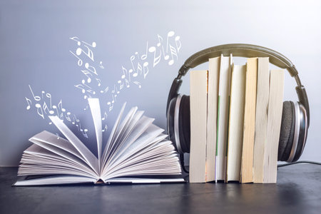 Black headphones on a stack of books near open book and flying notes. The concept of audiobooks