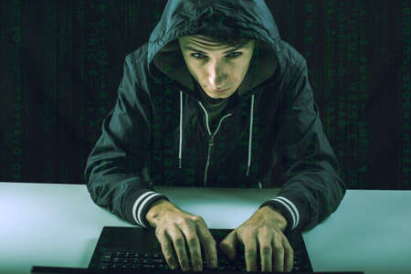 young hacker in the dark breaks the access to steal information and infect computers and systems. concept of hacking and cyber terrorismの写真素材