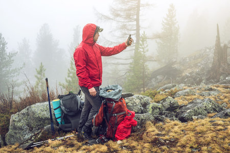 Hiker travels in the mountain forest in the mist with a backpack and trying to find a mobile connection or view the map on the gps. the concept of travel and Hiking in wild places of natureの写真素材
