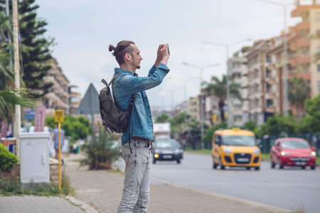 Man traveler with backpack makes a photo on your smartphone on a city street. The concept of connection and communication in the journey.の写真素材