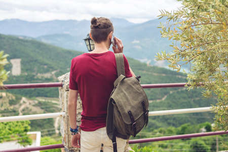 Man traveler with backpack talking on the phone on a background of mountains. The concept of connection and communication in the journey, roaming.の写真素材