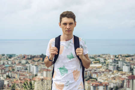 Man traveler with backpack explores the city looking at the panoramic view of the city and the coast. The concept of travel is discovering new placesの写真素材