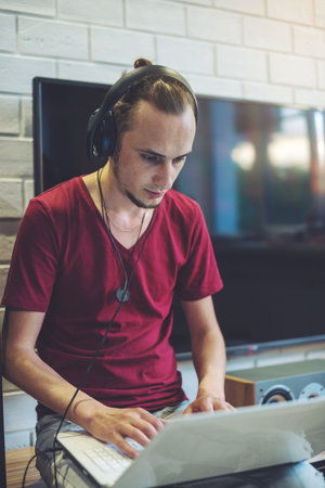 Young man in headphones listens to music and works at a laptop in a multimedia home atmosphere