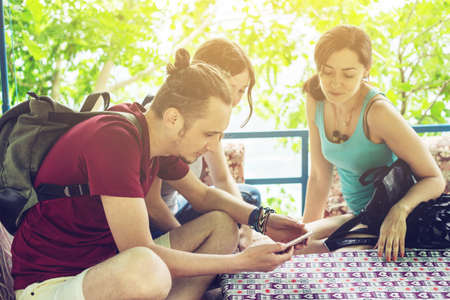 A group of young people relax outdoors in the gazebo and watch videos from your phone. Friends smile and laugh togetherの写真素材