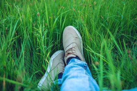 Youth sneakers on men legs in jeans on green grass. The concept of freedom and calmの写真素材