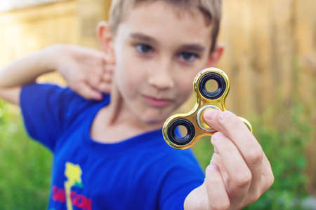 A boy plays with spinner twisting it in his hand on outdoors. Trends in children's anti-stress toys for attentionの写真素材