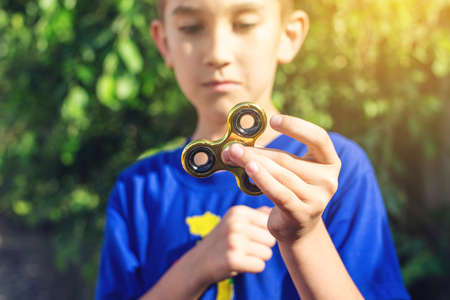 A boy plays with spinner twisting it in his hand on outdoors. Trends in children's anti-stress toys for attentionの写真素材