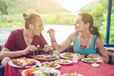 young couple eats vegetables and fish outdoors in a cozy restaurant on the water during travel, opens new kitchenの写真素材