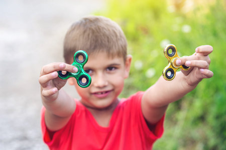 A boy plays with spinner twisting it in his hand on outdoors. Trends in children's anti-stress toys...