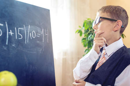 Back to school. Smart child solves a task in the classroom. Boy is writing on the blackboard. Concept for the first time in elementary schoolの写真素材
