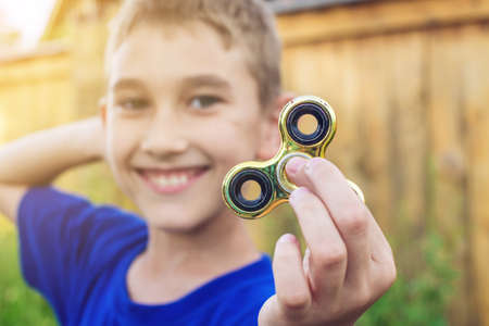 A boy plays with spinner twisting it in his hand on outdoors. Trends in children's anti-stress toys for attentionの写真素材