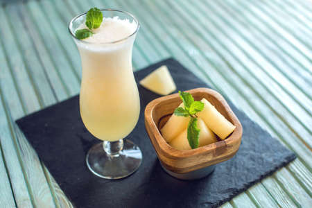 Fresh white smoothie in a glass with sliced pieces of melon and mint on a blue wooden background. Summer cool drinks at holidaysの写真素材