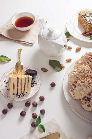 Beautifully decorated dessert table where the cake with meringue, layered pieces of cake and Cup of tea on a white table. Arrangement of delicious sweets, top viewの写真素材