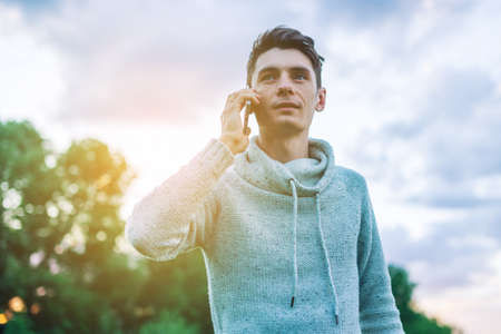 Young man businessman talking at mobile phone outside on a grass field at sunsetの写真素材
