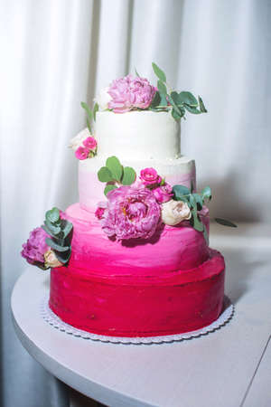 A beautiful home wedding four-tiered cake decorated with pink roses and green leaves in a rustic styleの写真素材