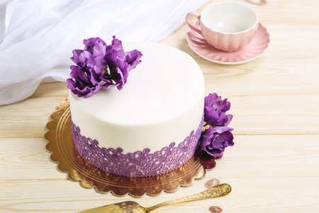 A beautiful home wedding cake decorated with purple peonies in a rustic style on wooden background.の写真素材