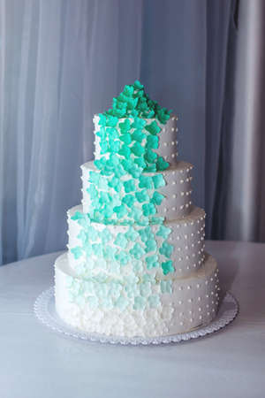 A beautiful home wedding four-tiered cake decorated with turquoise flowers on white tableの写真素材