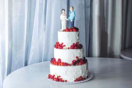 Beautiful wedding cake with figurines of the bride and groom on top decorated with strawberries on the tiersの写真素材